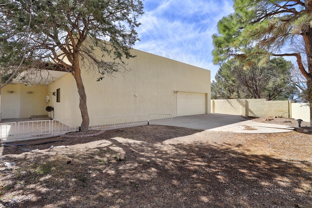 view of property exterior featuring stucco siding, concrete driveway, an attached garage, and fence