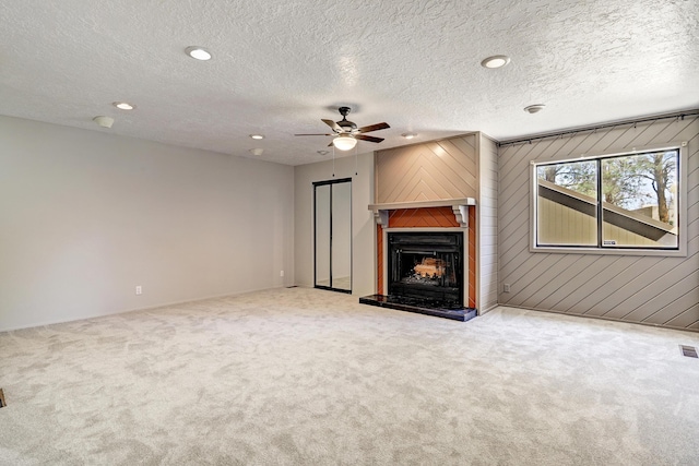 unfurnished living room featuring visible vents, carpet floors, a textured ceiling, and a fireplace with raised hearth