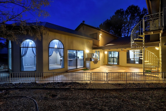 back of house at twilight with stairway, a patio area, and stucco siding