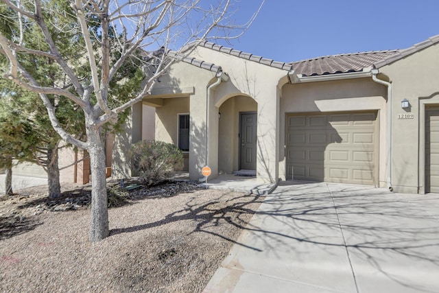 view of front facade with stucco siding, a tiled roof, an attached garage, and driveway