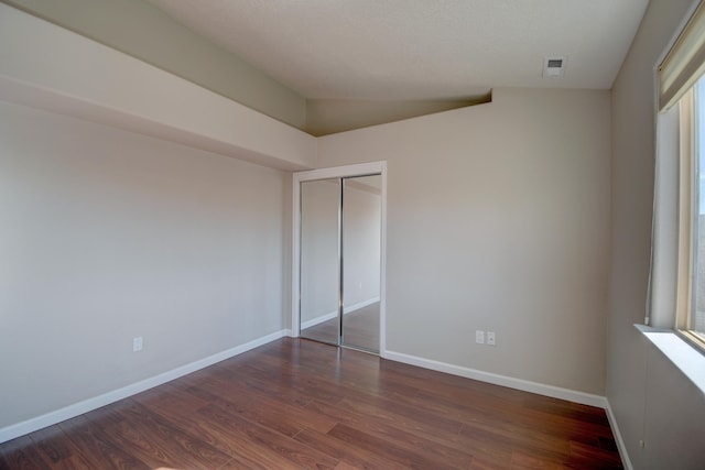 unfurnished bedroom with visible vents, baseboards, dark wood finished floors, vaulted ceiling, and a closet