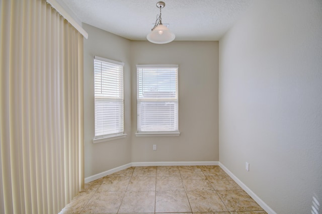 spare room with light tile patterned floors, baseboards, and a textured ceiling