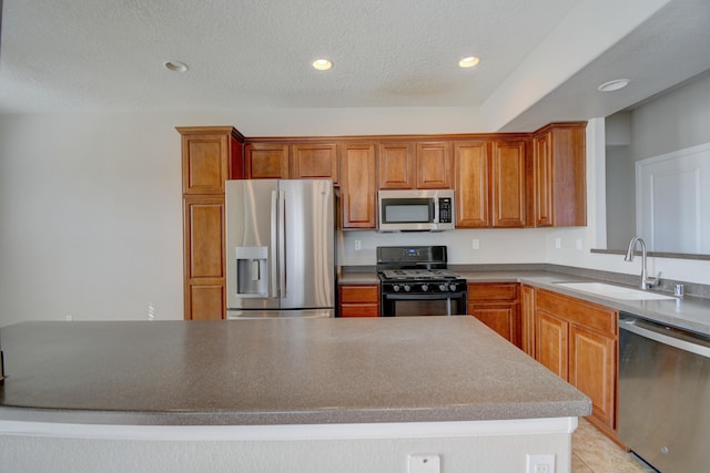 kitchen featuring recessed lighting, a sink, appliances with stainless steel finishes, a textured ceiling, and brown cabinets