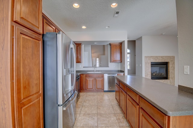 kitchen with a tiled fireplace, light tile patterned floors, appliances with stainless steel finishes, a textured ceiling, and a sink