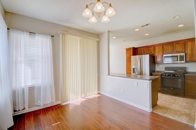 kitchen featuring visible vents, light wood-style flooring, a peninsula, appliances with stainless steel finishes, and brown cabinetry