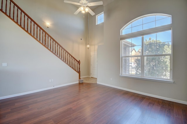 unfurnished living room with stairs, a high ceiling, wood finished floors, and baseboards