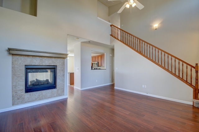 unfurnished living room with baseboards, a tiled fireplace, stairway, a high ceiling, and wood finished floors