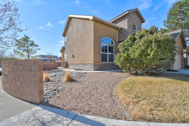 view of side of home featuring stucco siding, stone siding, and fence