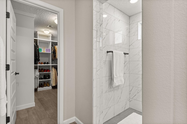 bathroom with a spacious closet, a textured ceiling, walk in shower, and wood finished floors