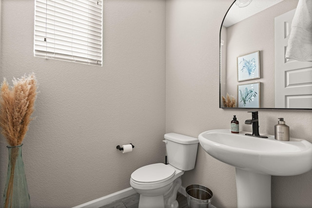 bathroom featuring toilet, baseboards, and a textured wall