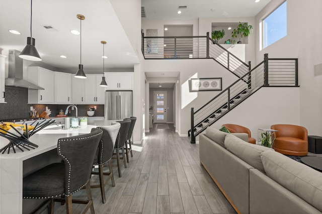 living room featuring recessed lighting, light wood-style floors, baseboards, a towering ceiling, and stairs