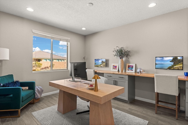 office area featuring a textured ceiling, built in study area, baseboards, and wood finished floors