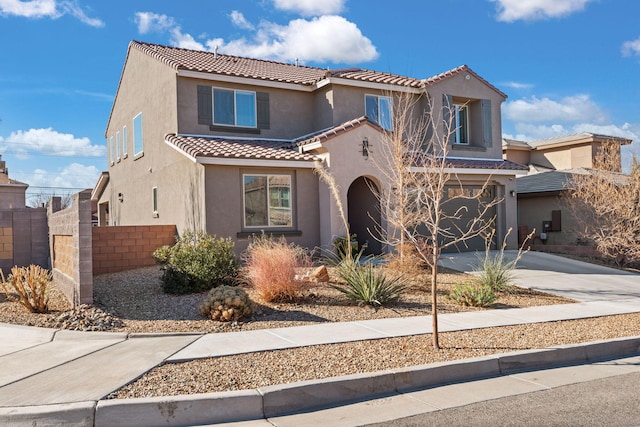 mediterranean / spanish-style home with stucco siding, driveway, a tile roof, fence, and an attached garage