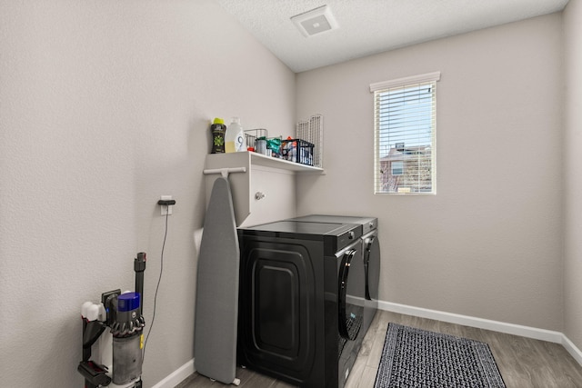 washroom with baseboards, light wood finished floors, laundry area, a textured ceiling, and washer and dryer