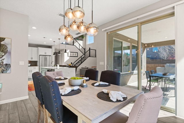 dining room featuring visible vents, baseboards, a chandelier, stairway, and light wood-style floors