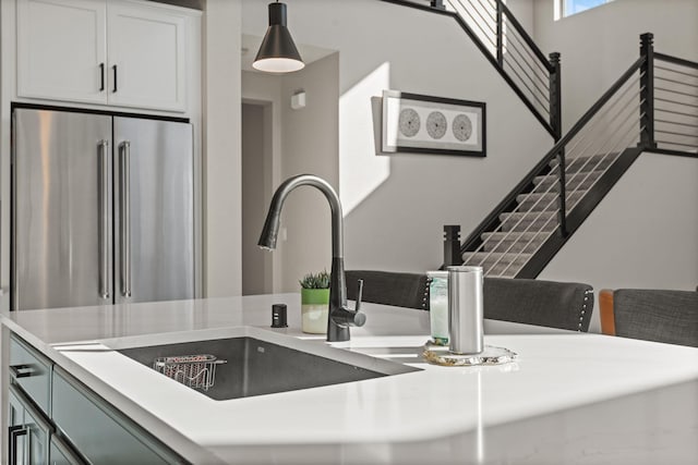 interior space featuring pendant lighting, light countertops, high end fridge, white cabinetry, and a sink