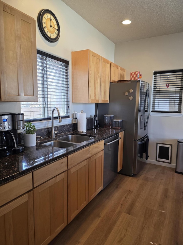 kitchen with a sink, dark stone countertops, a textured ceiling, stainless steel appliances, and dark wood-style flooring