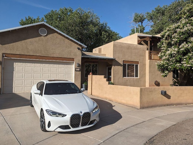 pueblo revival-style home featuring concrete driveway, an attached garage, and stucco siding