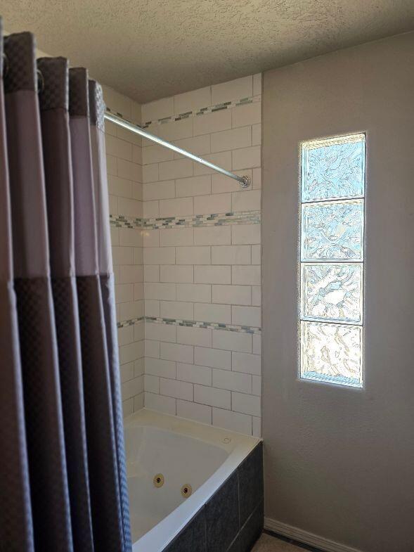 full bathroom with baseboards, a textured ceiling, and a combined bath / shower with jetted tub