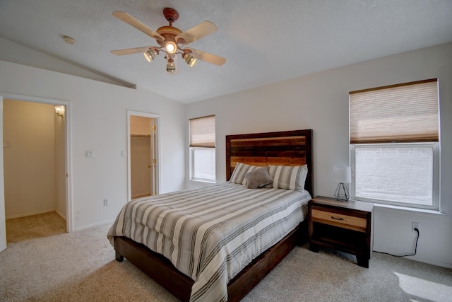 bedroom featuring carpet, lofted ceiling, ceiling fan, a textured ceiling, and a walk in closet