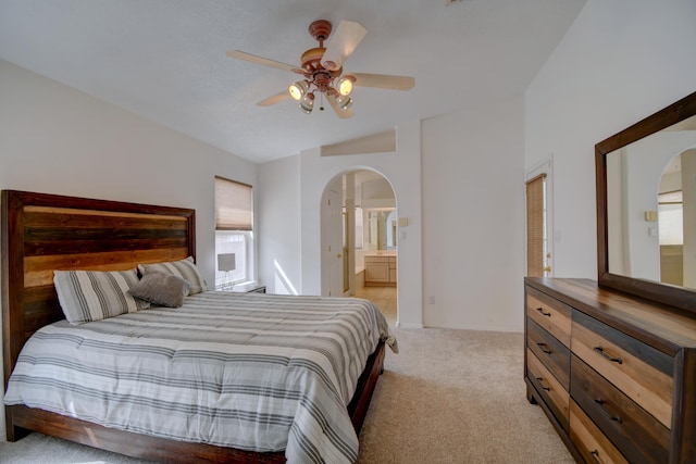 bedroom featuring arched walkways, light colored carpet, ensuite bath, and a ceiling fan