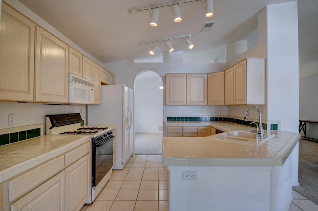 kitchen featuring light brown cabinetry, a sink, gas range oven, arched walkways, and white microwave