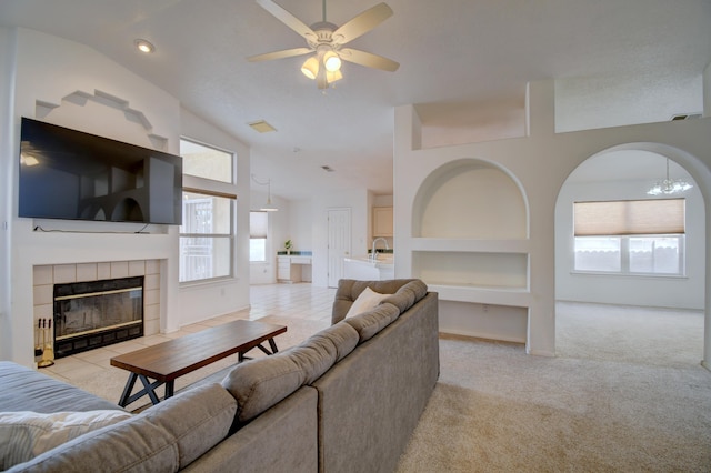 living area featuring built in features, a fireplace, lofted ceiling, light colored carpet, and ceiling fan