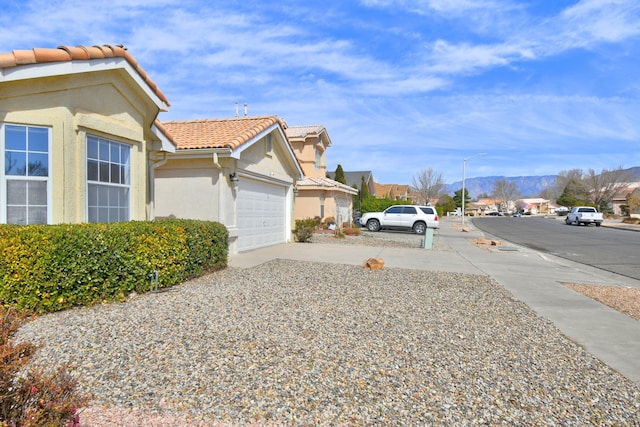 view of side of home with driveway, stucco siding, a garage, a tile roof, and a residential view