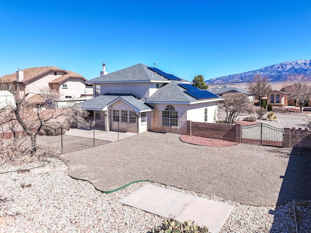 rear view of property featuring stucco siding, a gate, roof mounted solar panels, fence private yard, and a patio area