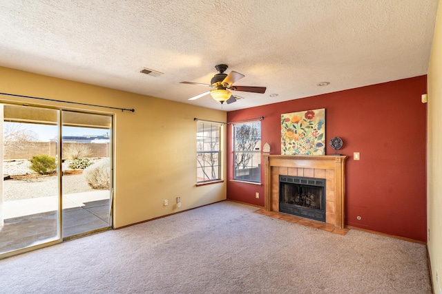 unfurnished living room with a tiled fireplace, carpet, a healthy amount of sunlight, and visible vents