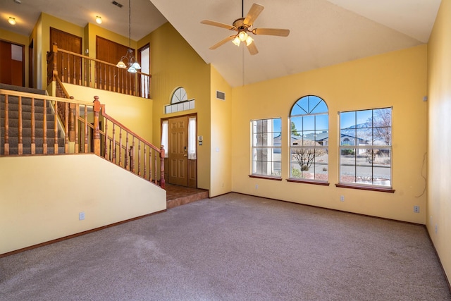 carpeted entryway with visible vents, high vaulted ceiling, ceiling fan with notable chandelier, baseboards, and stairs