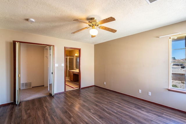 unfurnished bedroom featuring baseboards, visible vents, dark wood finished floors, ensuite bath, and ceiling fan