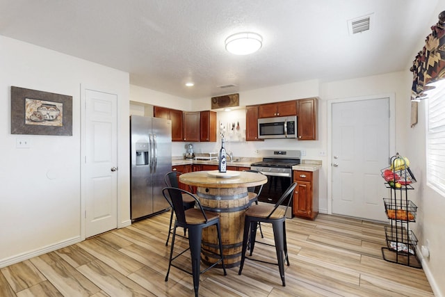 kitchen featuring light wood finished floors, visible vents, baseboards, light countertops, and stainless steel appliances