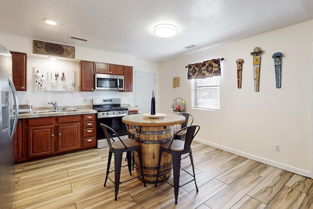 kitchen with visible vents, light wood-style flooring, stainless steel appliances, and a sink