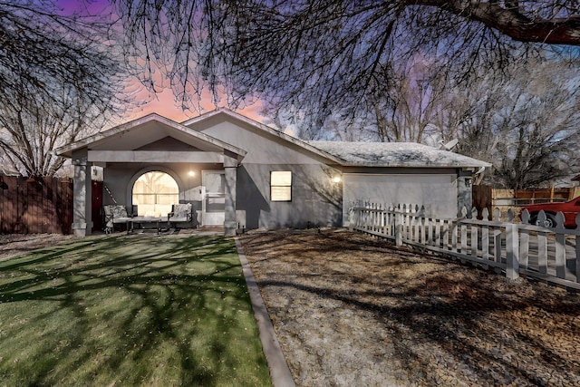 view of front of house with stucco siding, a yard, and fence