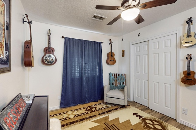 sitting room featuring a ceiling fan, baseboards, wood finished floors, visible vents, and a textured ceiling