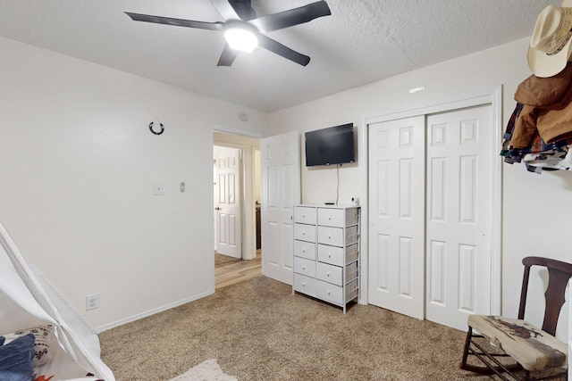 bedroom featuring a textured ceiling, a closet, baseboards, light colored carpet, and ceiling fan