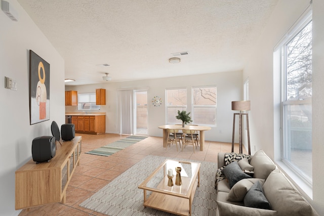 living area featuring visible vents, a textured ceiling, a healthy amount of sunlight, and light tile patterned flooring