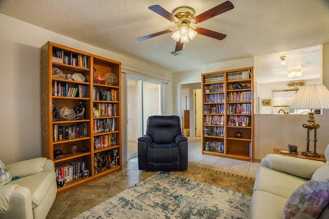 living area with tile patterned flooring, visible vents, a textured ceiling, and ceiling fan