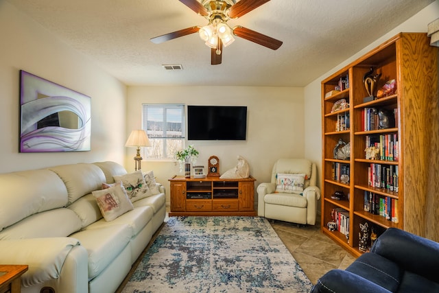 living area with tile patterned floors, visible vents, a textured ceiling, and a ceiling fan