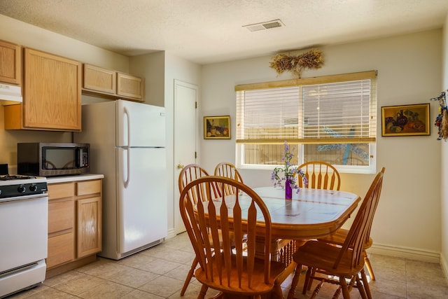 kitchen featuring visible vents, light brown cabinets, under cabinet range hood, a textured ceiling, and white appliances