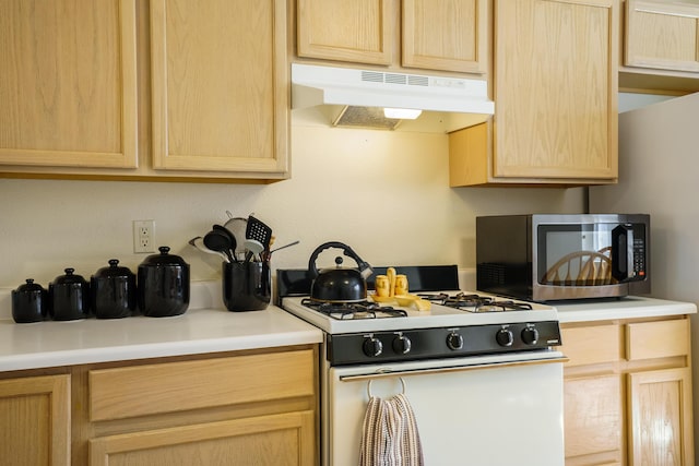 kitchen featuring white gas stove, light brown cabinetry, light countertops, under cabinet range hood, and stainless steel microwave