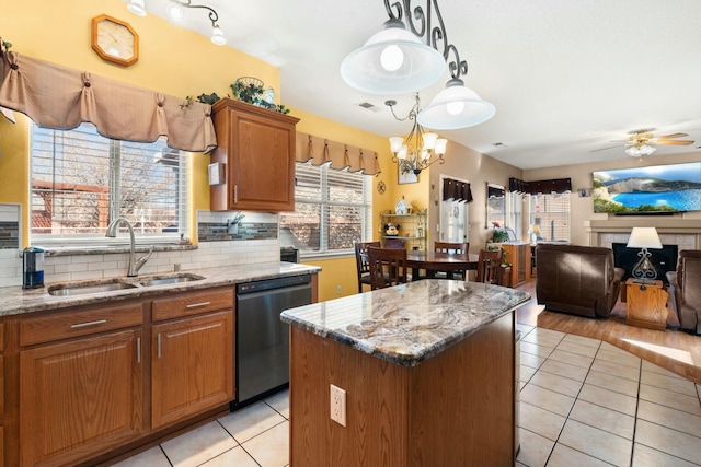 kitchen with light stone countertops, a sink, stainless steel dishwasher, backsplash, and a center island