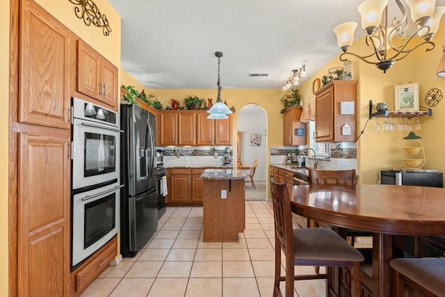 kitchen featuring a kitchen island, light tile patterned floors, decorative backsplash, appliances with stainless steel finishes, and an inviting chandelier