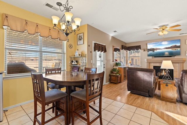 dining room featuring light tile patterned floors, ceiling fan with notable chandelier, visible vents, and a tile fireplace