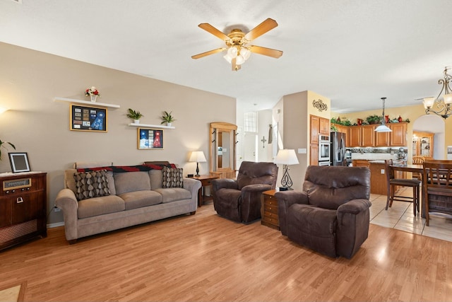 living room with arched walkways, light wood-style floors, and ceiling fan