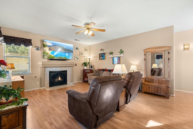 living room with visible vents, light wood-style floors, baseboards, ceiling fan, and a tile fireplace