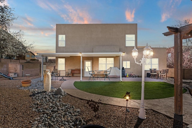 back of property at dusk with a yard, a patio area, fence, and stucco siding