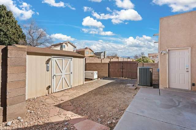 view of yard with fence, central air condition unit, an outbuilding, a storage unit, and a gate