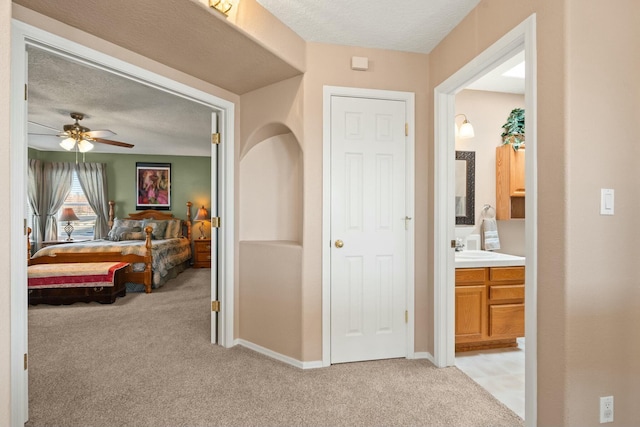 hallway with a textured ceiling, baseboards, and light carpet